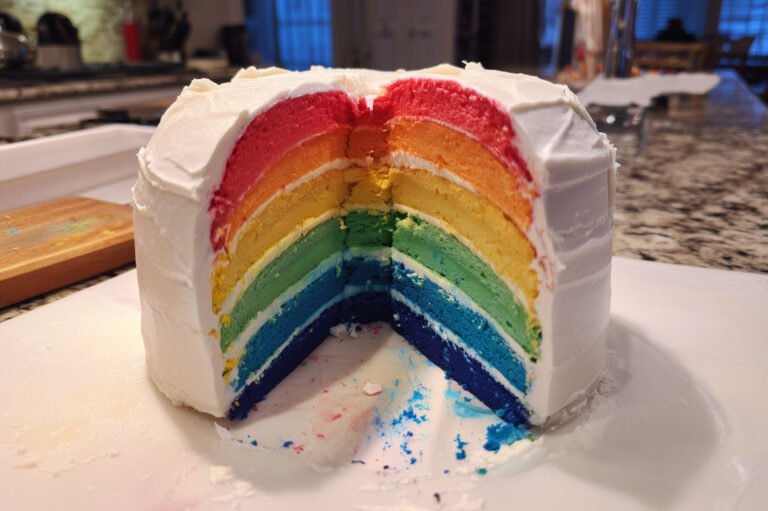 Un rainbow cake tranché avec un glaçage blanc